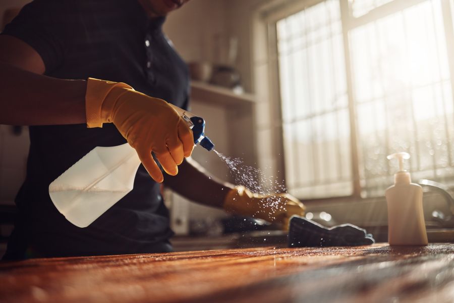 House cleaner spraying disinfectant on kitchen counter in a sunlit home kitchen